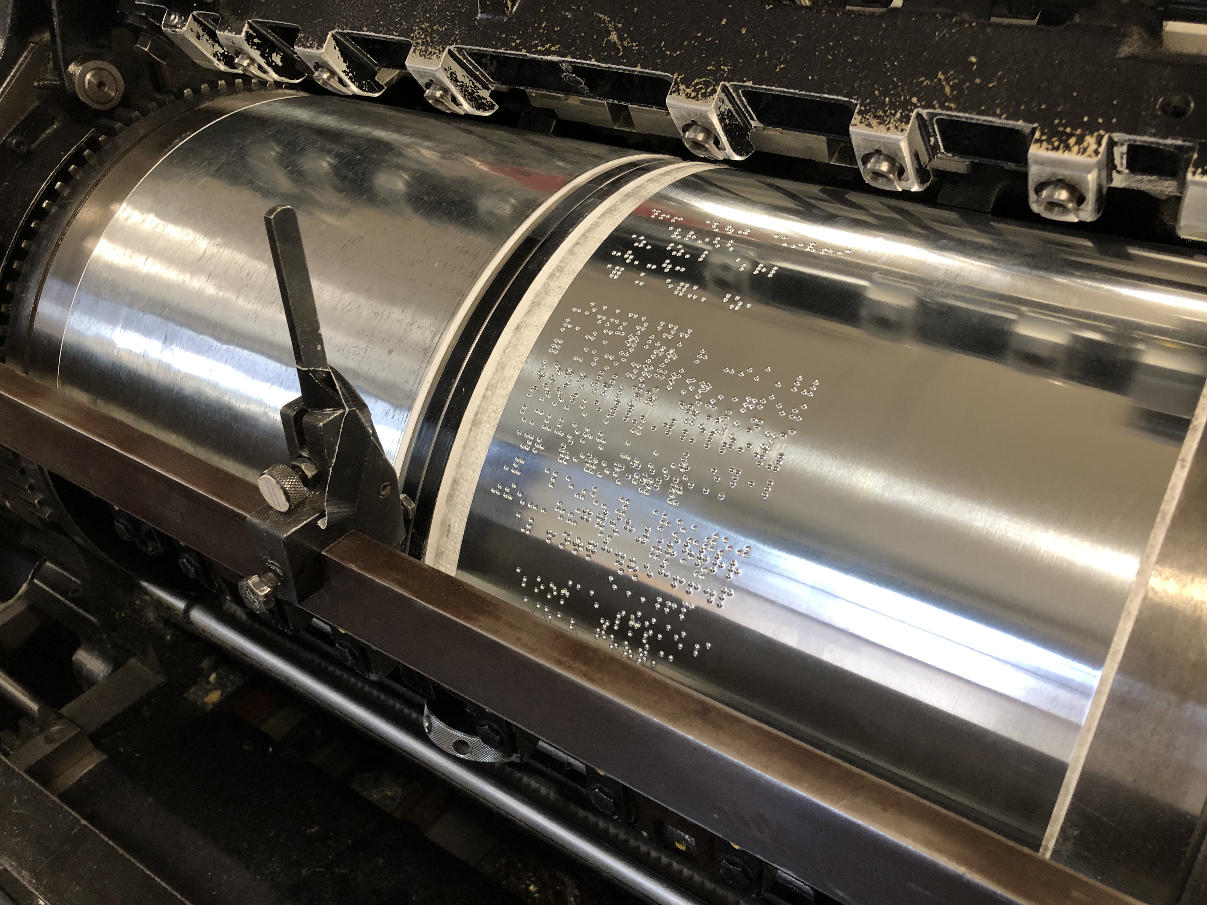 A close-up of the metal cylinders in the Heidelberg braille printing press, which has braille dots engraved on it, to be embossed on paper.