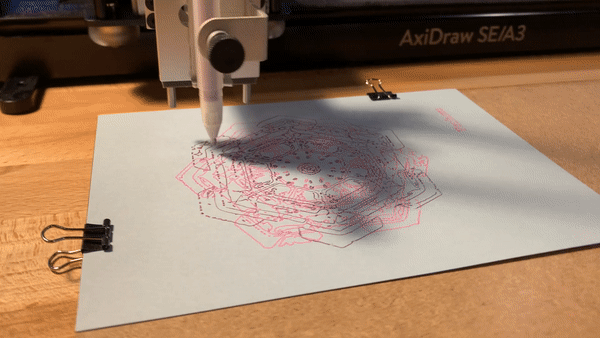 A pink and silver snowflake being drawn onto a gray piece of paper. The AxiDraw raises and lowers a pen attached to the arm of the machine to add ink dots across the card to complete the snowflake design being drawn.